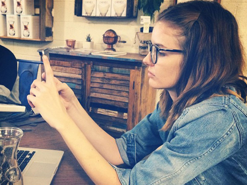 A girl having relationship problems at a coffee shop going through her boyfriend's text messages.