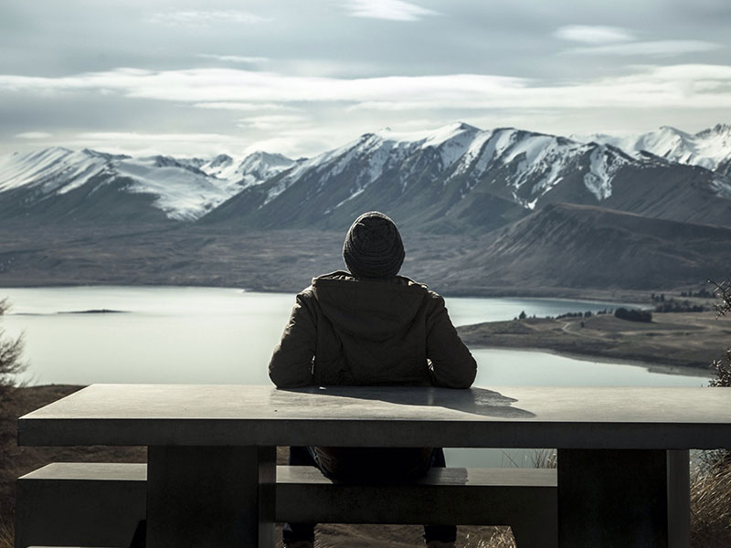 A man having relationship problems sitting alone in front of a mountain to get some me time.