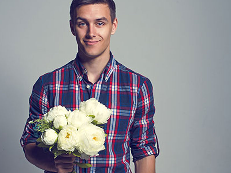 A guy smiling and holding flowers for a date.
