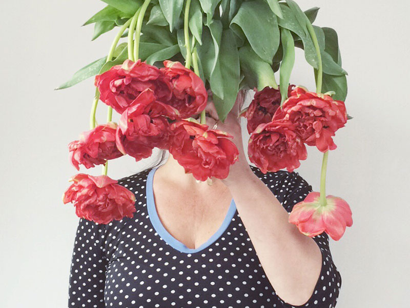 A single woman who's alone on Valentines Day holding sad looking flowers in front of her face.