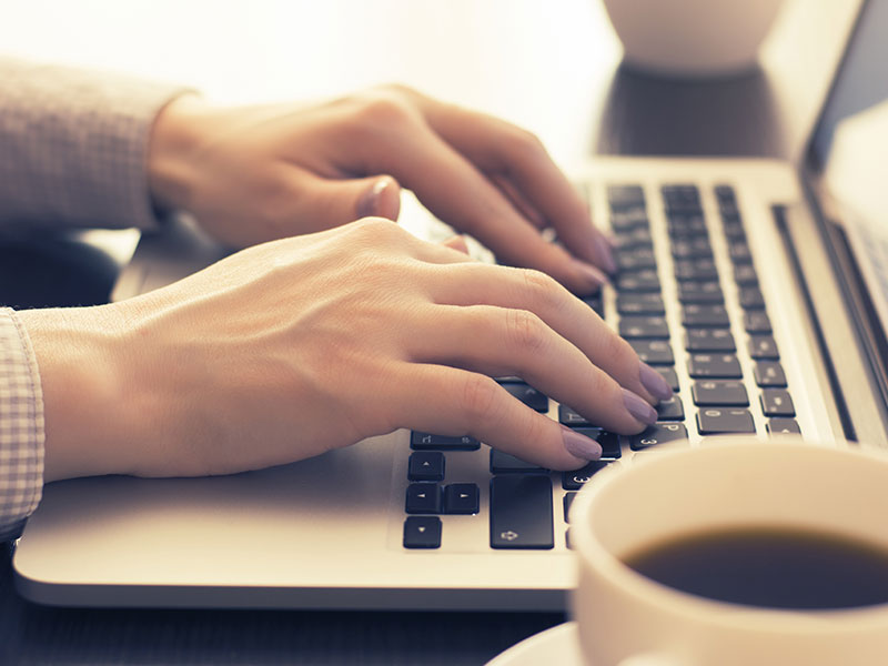 A woman with purple nail polish starting a conversation online while typing on her laptop.
