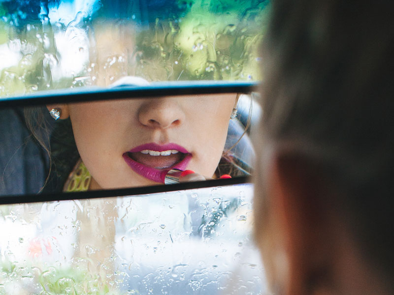 A strong woman with attitude putting her lipstick on in the car.
