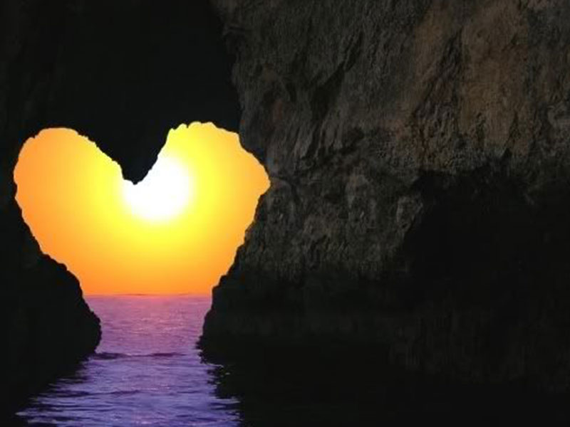 A picture of a rock cut out in the shape of a heart and the sunset shining through.