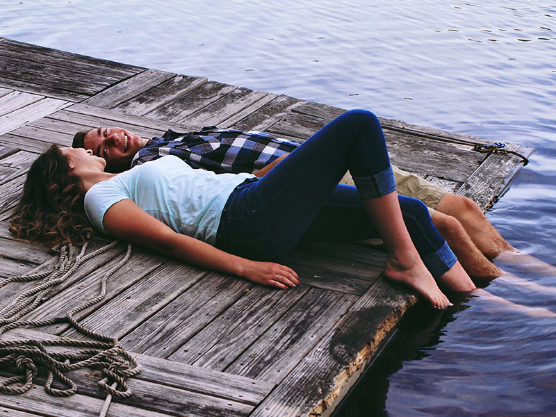 A couple having the relationship talk while laying on a dock with their feet in the water.