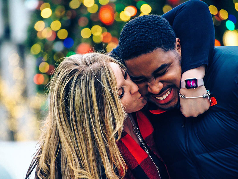 A couple hugging and kissing in front of a Christmas tree.