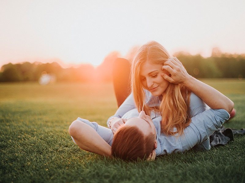 A couple in an open relationship cuddling in some grass.