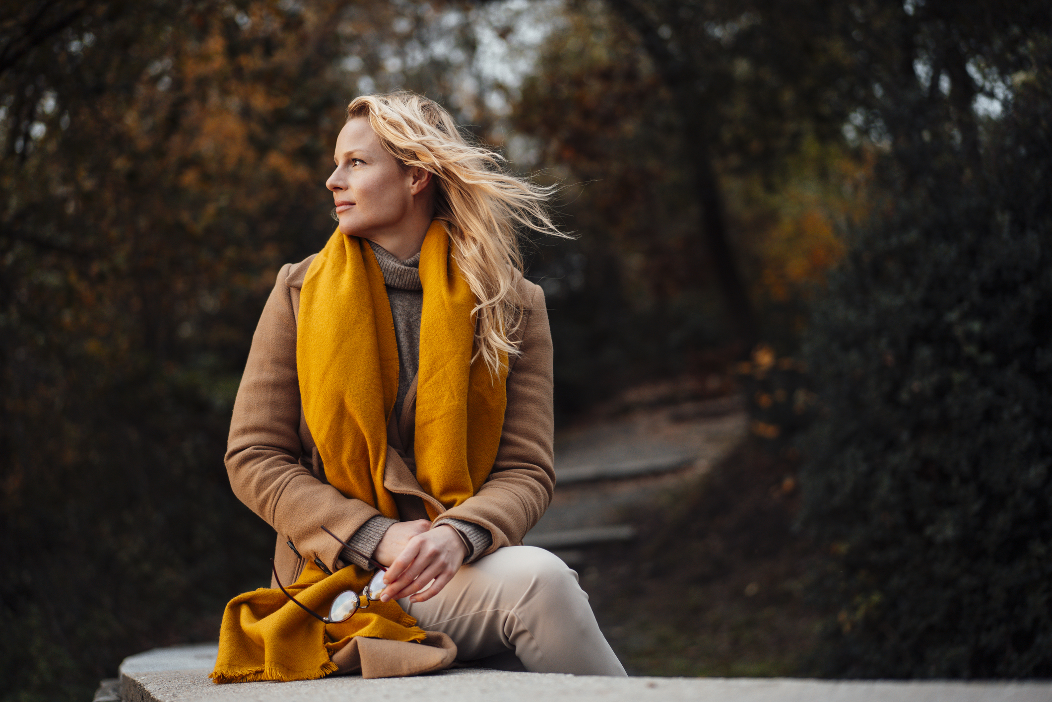Blonde woman sitting outdoors and looking out into the distance while thinking about how to break up with someone you love.