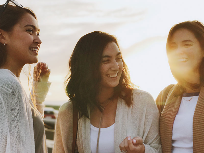 A group of sisters--oldest, middle, youngest-laughing together on a beach.