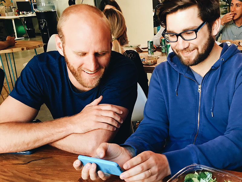 Two men reading a dating message together on one of their phones.