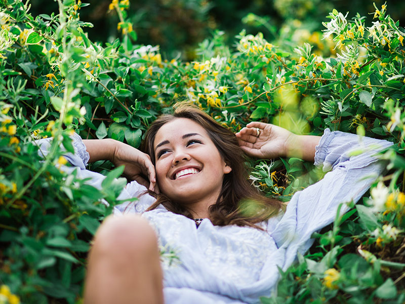 A woman who got over being unlucky in love, laughing in a pile of flowers and grass because now she's happy.