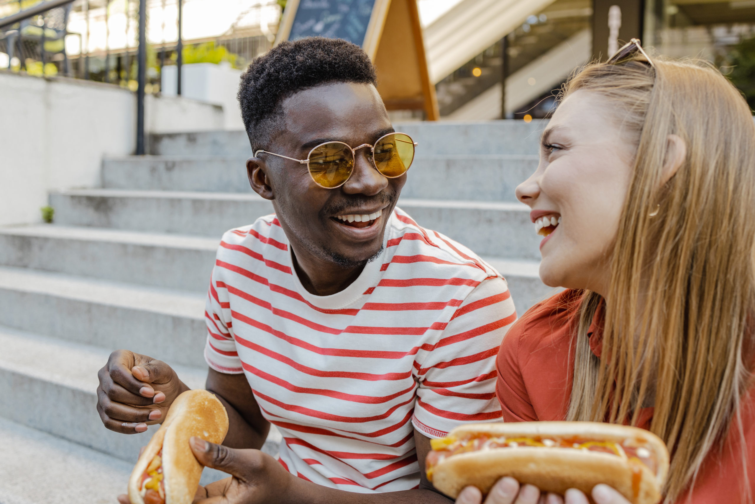 Young African American man and Caucasian woman on a first date, eating a hot dog on the street and laughing while getting over their first date nerves.