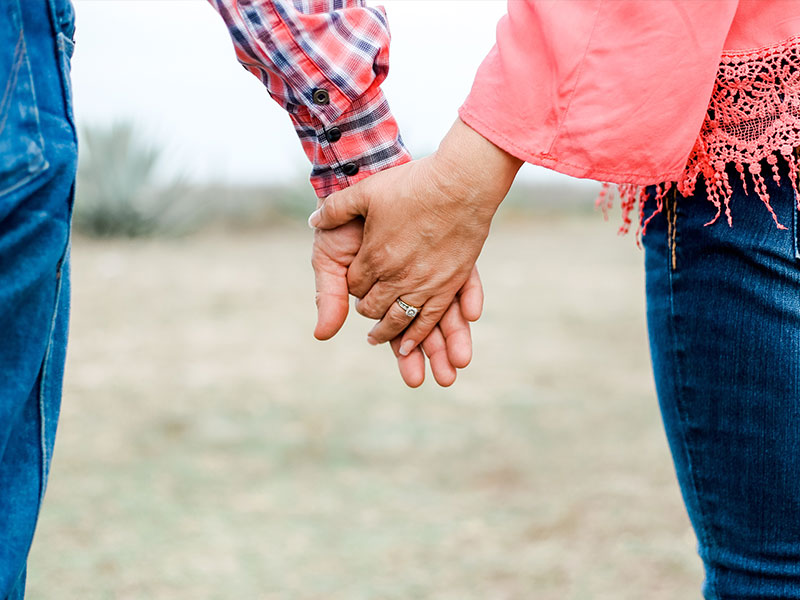 A cheating partner walking through a field holding hands with her husband.