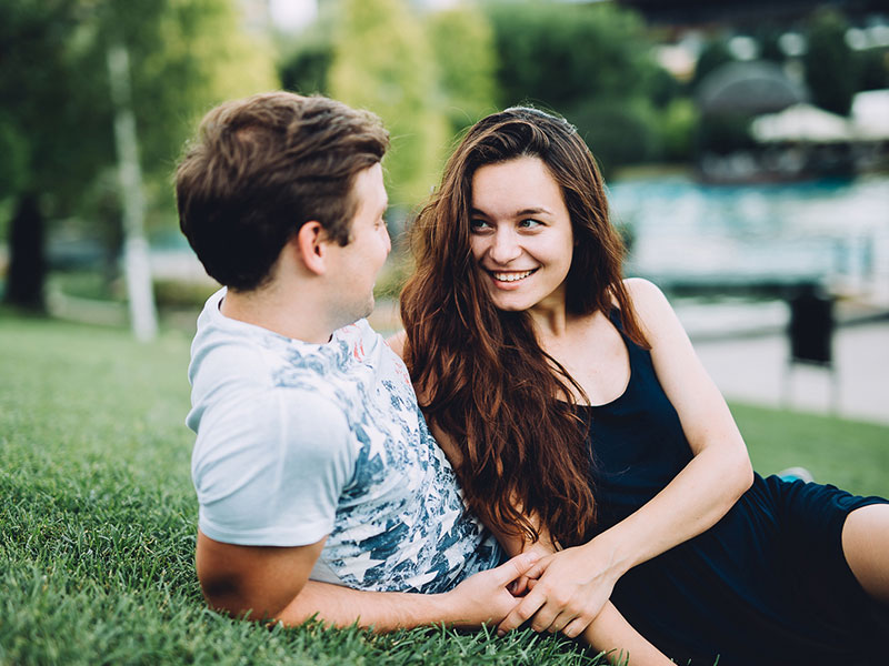 A guy who's wondering do girls like shy guys, sitting on the grass with a girl who's flirting with him.