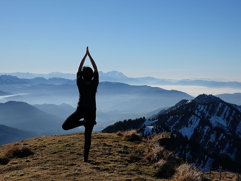 A woman who's learning to love herself again doing yoga on a mountaintop.