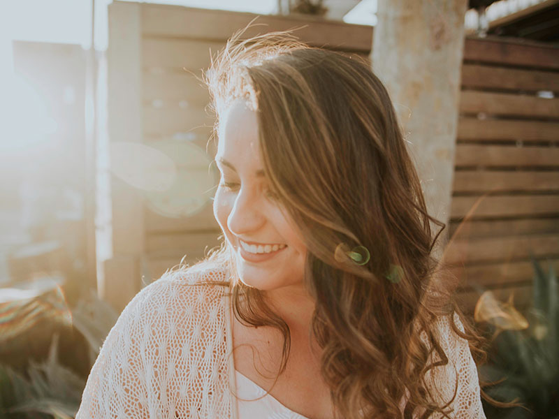A woman who knows the difference of being alone vs lonely smiling in the sun by herself.