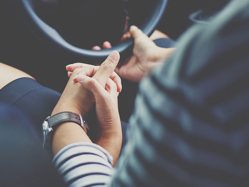 A controlling boyfriend holding his girlfriend's hand while he drives.