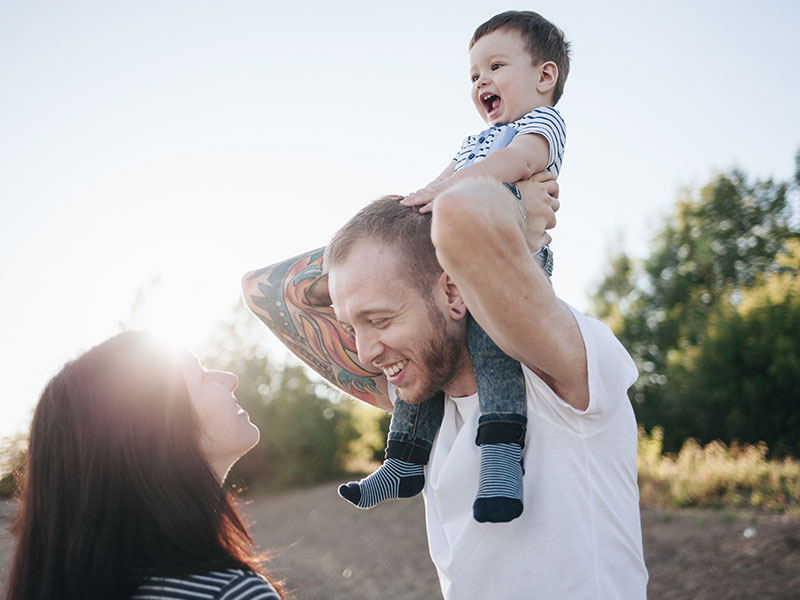 A man who wants to know how to be a better husband, holding his son and laughing while looking at his wife.