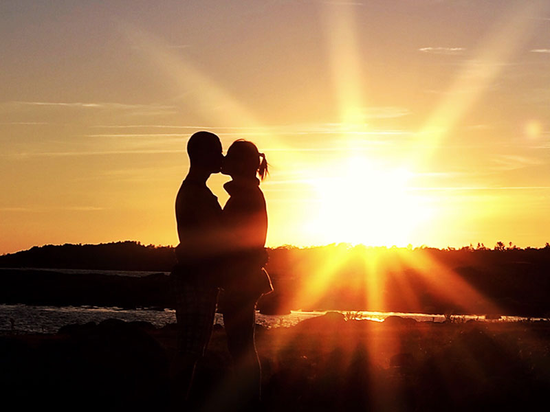 A couple standing in front of a sunset, sharing a kiss on a first date.