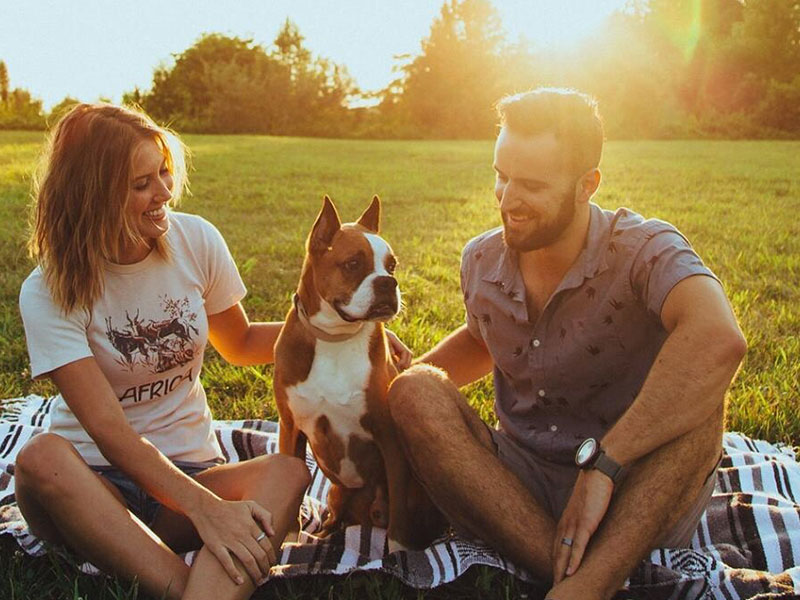 A couple following these first date rules while sitting with a dog on a blanket at the park.