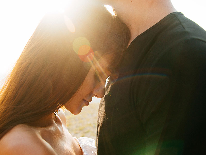 A couple in a healthy relationship hugging in the sunset as the woman closes her eyes and smiles.