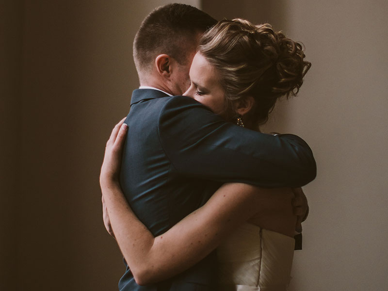 A couple that wanted to learn how to fix a relationship once it's broken, hugging at a wedding with their eyes closed.