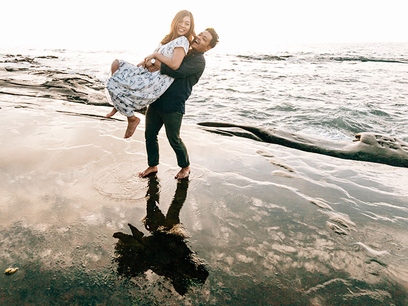 A couple that took this relationship advice, laughing and flirty on the beach at sunset.