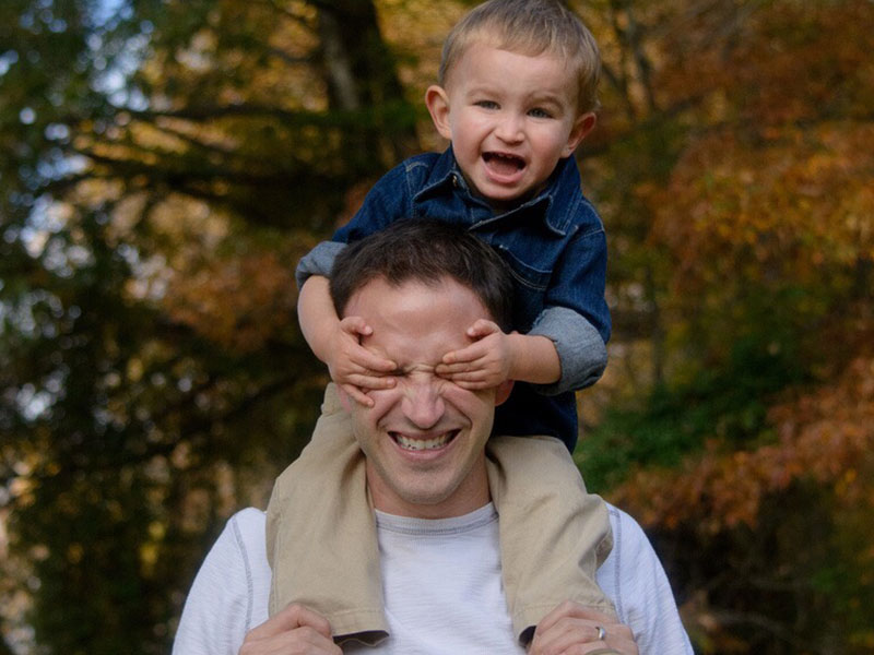 A single dad laughing as he holds his son on his shoulders.