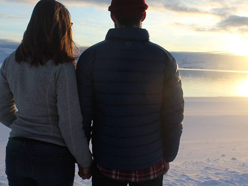 A couple who's falling out of love, standing on the beach together thinking.