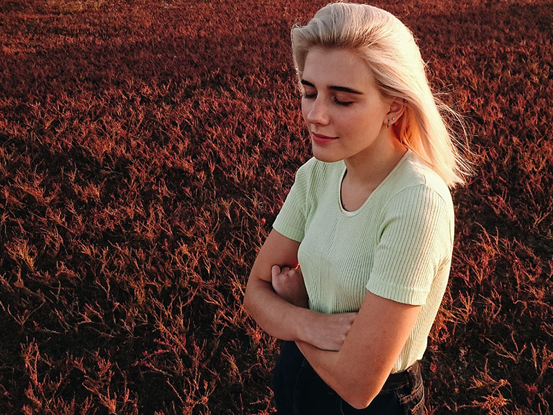 A woman hugging herself in a field and thinking after learning how to move on after being cheated on.
