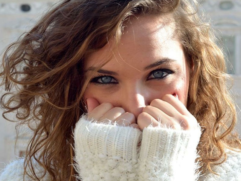 A woman who's showing some of this body language of women, smiling behind her hands.