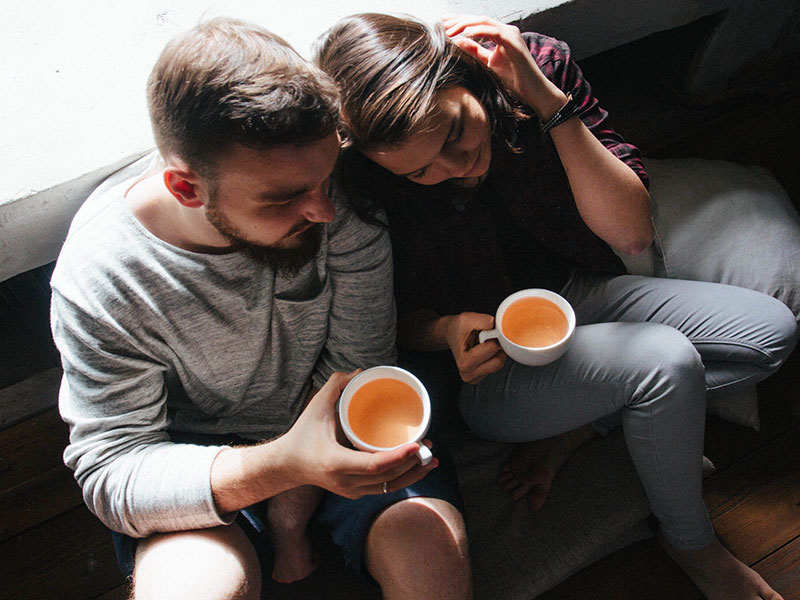 A woman wondering "Do I love him?" as she cuddles up with her boyfriend as they drink tea.
