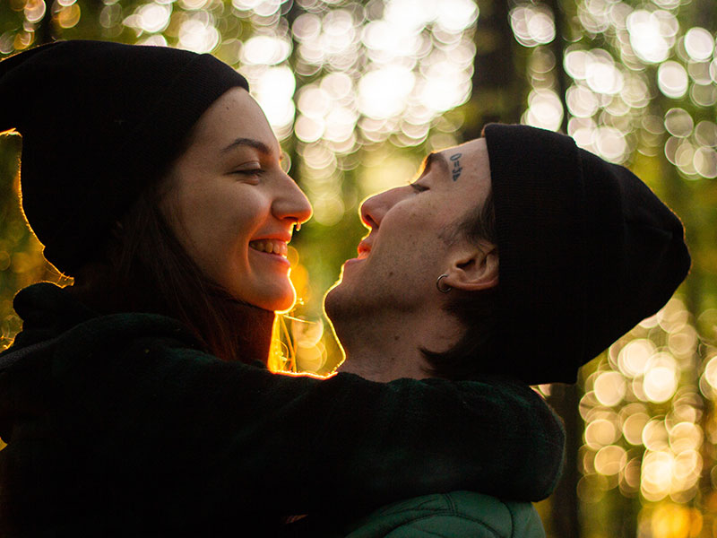 A couple who's good at emotional engagement, hugging and smiling at each other in the woods.