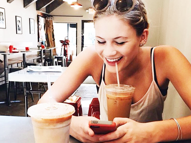 A woman who learned how to use Tinder, at a coffee shop laughing while she swipes on guys.