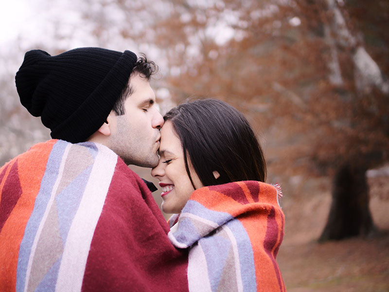 A man who used to have a lot of relationship insecurities kissing his girlfriend's head and smiling as they snuggle together in a blanket.