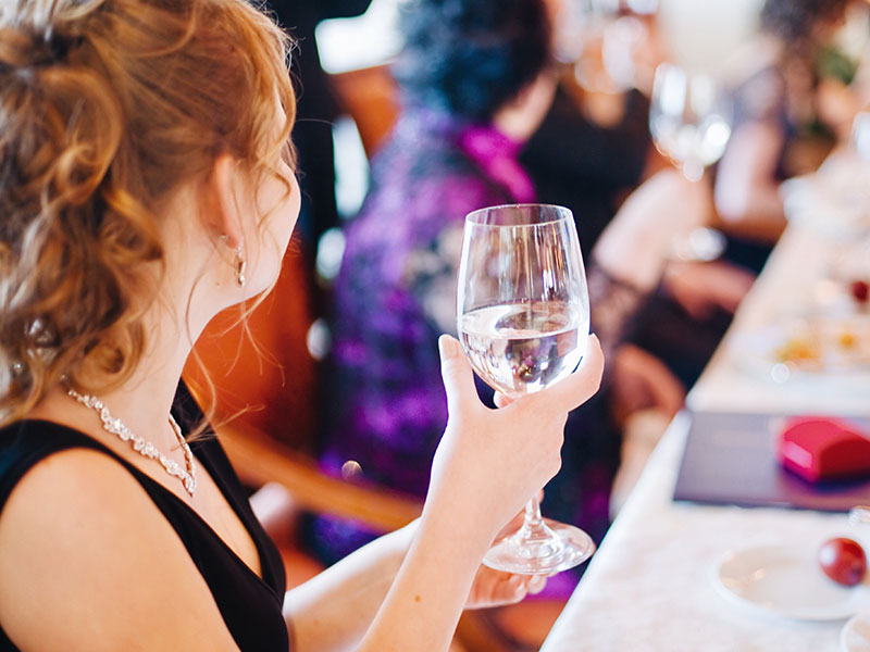 A girl who knows what going stag means, sitting alone at a wedding and cheersing the people around her.