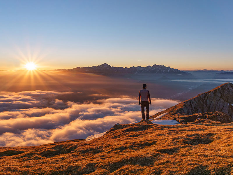 A guy who learned what to do after a breakup, standing on top of a mountain he just climbed up looking proud and reflective.