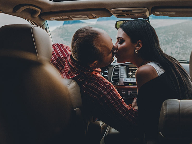 A couple who used these couple date ideas, kissing in their car during a road trip.