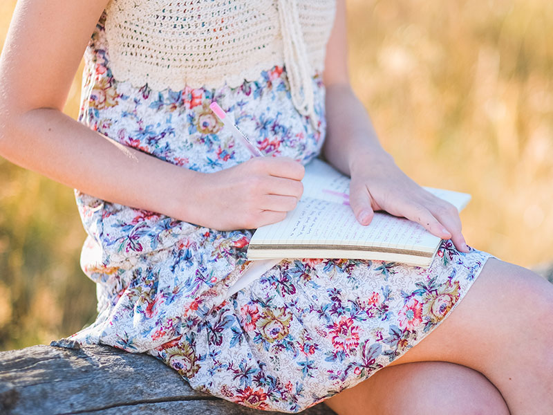 A woman using these breakup letter examples to write her own breakup letter while sitting in a field outside.