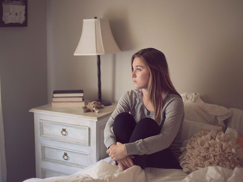 A girl who wants to know how to stop liking someone, sitting in bed thinking about a crush who doesn't like her back.