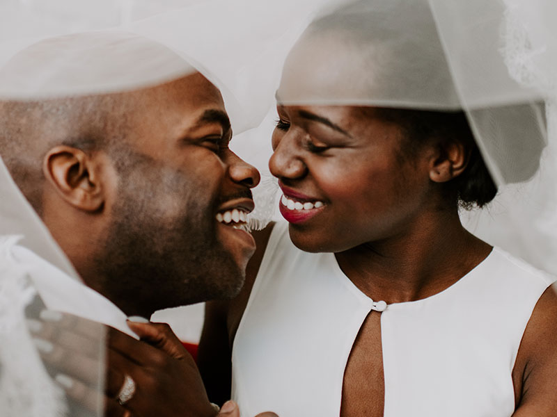 A man and woman who know what it's like to marry your best friend, dressed up for their wedding laughing as they're about to kiss.