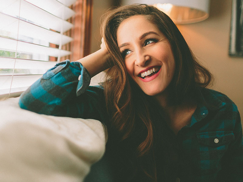 A woman who's thinking about leaving her ex, laughing on a couch.