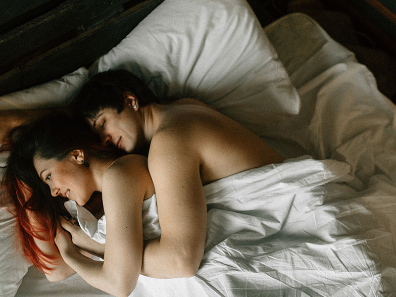 A couple that uses enthusiastic consent to enhance intimacy lying in bed together smiling.