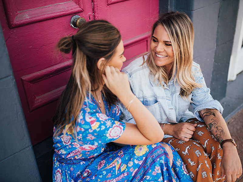 A woman who's trying to learn how to be more social, talking to a friend one on one on a front porch stoop.
