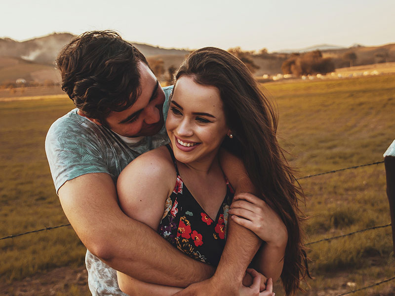 A couple that listened to this love advice, smiling and laughing in a field together as they hug.
