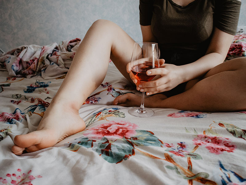 A woman who's alone on a Friday night, drinking wine in bed.