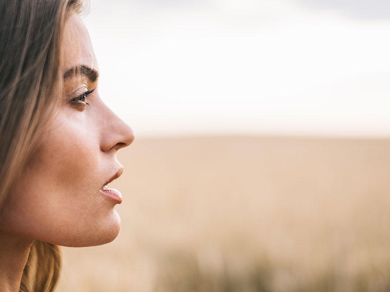 A woman who's battling with codependency standing in a field thinking.