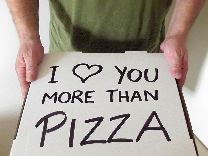 A man holding a pizza box that says, "I heart you more than pizza." One of the romantic gestures for her that will make her day.