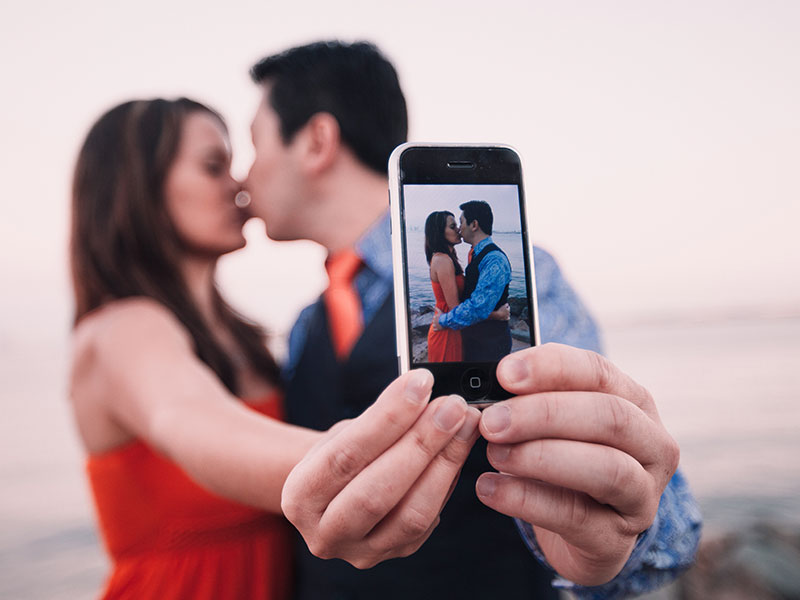 A couple taking a selfie while kissing, displaying an example of what social media and relationships.