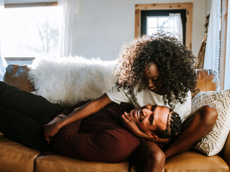 A couple in true love, laughing and cuddling on the couch.