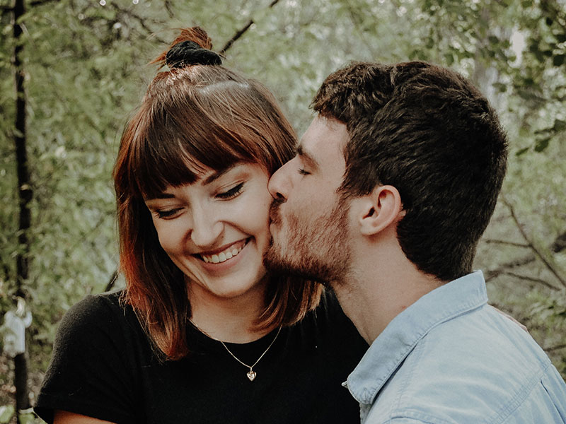 A guy kissing the cheek of his jealous girlfriend, and explaining she has nothing to worry about.